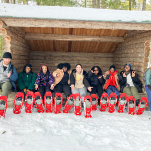 Alternative Spring Break BIPOC students wearing snowshoes at a lean-to at Camp Dudley in Westport, New York