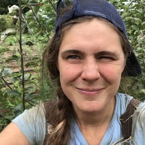 Courtney Grimes-Sutton of Mace Chasm Farm in front of young trees in the farm's nursery